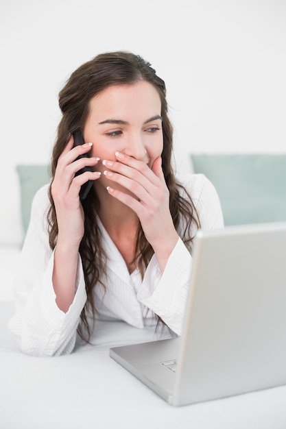 Casual woman using cellphone and laptop in bed