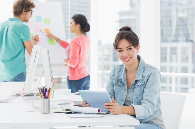 Casual woman using digital tablet with colleagues behind in office