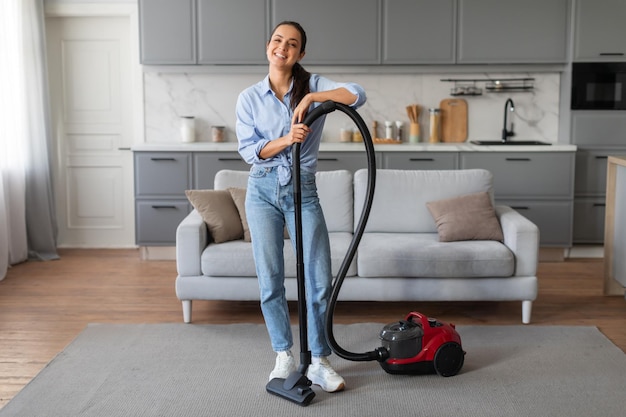 Casual woman vacuuming rug enjoying chores at home