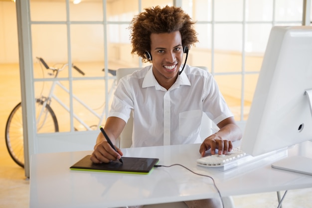 Casual young businessman using digitizer and headset at desk