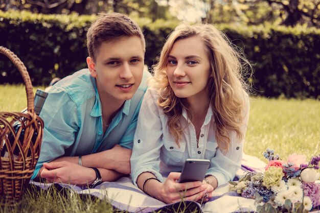 Casual young couple relaxing on a lawn and looking photos on smartphone.