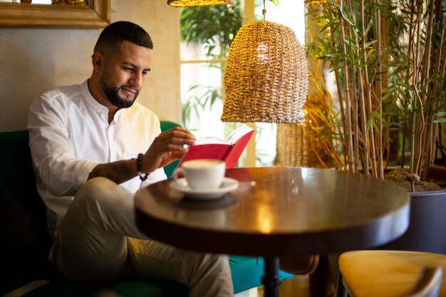 朝のコーヒーを飲みながら本を読んでいるカジュアルな若いラテン系男性。