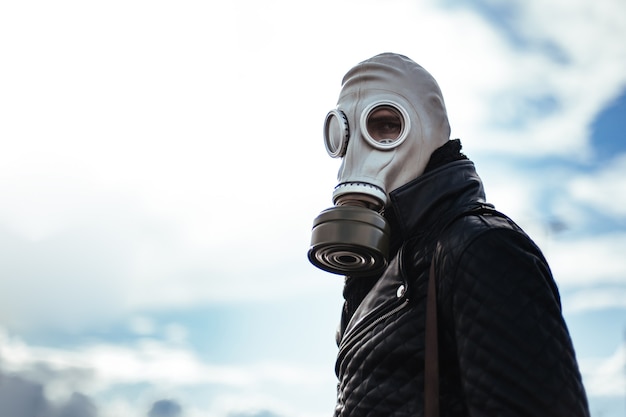 空の街の通りに立っている防毒マスクのカジュアルな若い男。コピースペース付きの写真