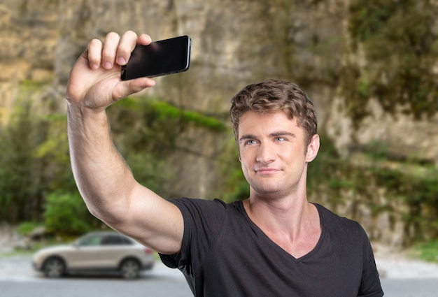 Casual young man tourist taking selfie in a journey using his smartphone