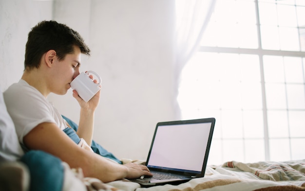 Casual young man using laptop in bed at home