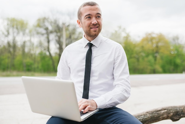 Casual zakenman dragen wit overhemd typen op zijn computer maken verslag van zijn bedrijf met behulp van draadloze knappe man aan het werk op laptop buiten in het park technologie en bedrijfsconcept