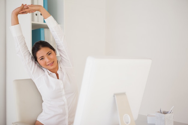 Casual zakenvrouw die zich uitstrekt op haar bureau