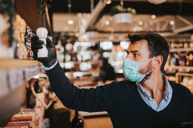 Casually dressed middle age man with face protective mask and gloves buying healthy food and drink in a modern supermarket or grocery store. Pandemic or epidemic lifestyle.