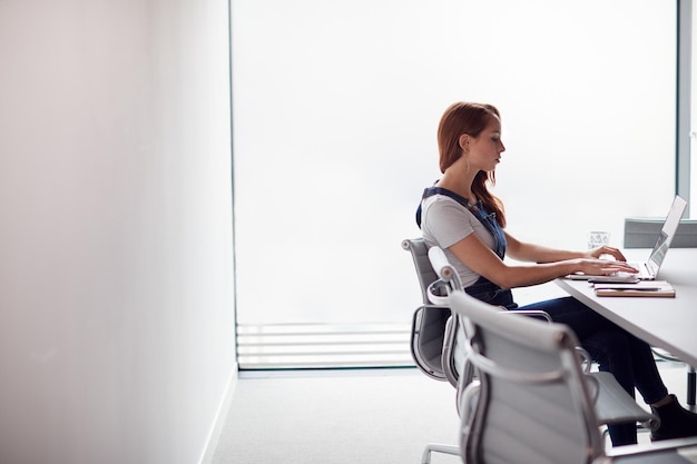 Photo casually dressed young businesswoman working on laptop at desk in modern workplace