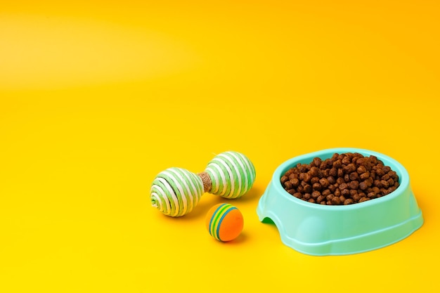 Cat bowl with dry food and toys on yellow background studio shot