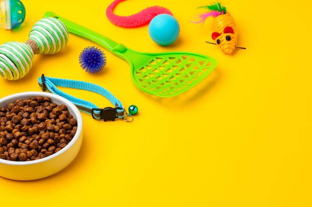 Cat bowl with dry food and toys on yellow background studio shot