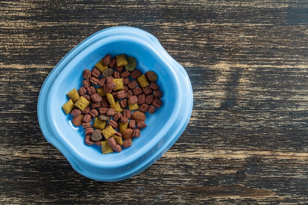 Cat food in a blue plastic bowl on wooden background top view copy spase