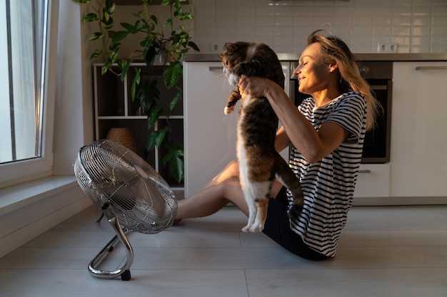 Cat hates stream of cold air and tries to run away from fan and\
landlady sitting on floor in kitchen