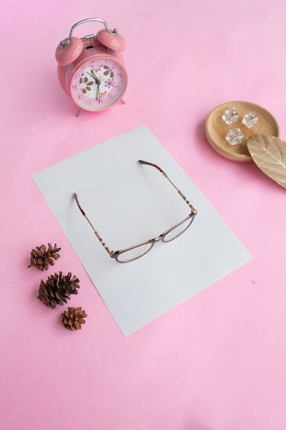 Cat's eye glasses in the photo from above with a minimalist concept on a purple paper background with an alarm clock decoration and dry leaves