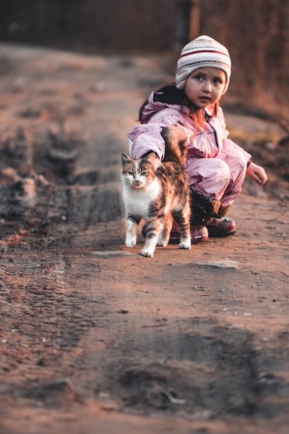 Cat walks with a little girl in the park. walk with the animal in the fall. cat plays in the leaves