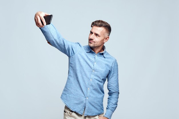 Catching happy moments cheerful and handsome bearded man in casual wear making selfie while standing