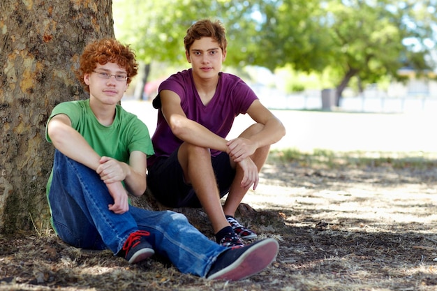 Foto prendere un po' d'ombra in una calda giornata inquadratura di due adolescenti che si rilassano all'ombra di un albero nel parco