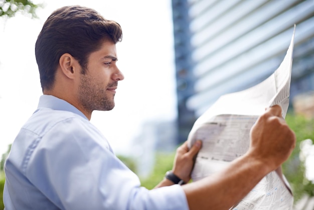 Catching up on the news A handsome young businessman reading a newspaper while sitting on a bench in the city