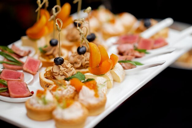 Catering. Colorful meat snacks with bread fruits and vegetables on a white plate. . High quality photo