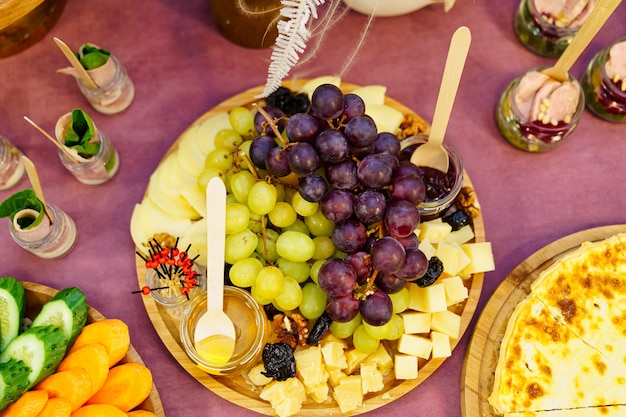 Photo catering. wooden plate with grapes, cheese, jam and honey in small glass jars.