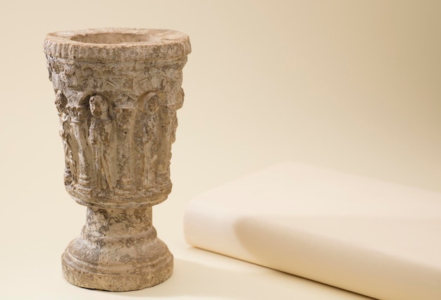 католическая, каменная чаша с библией рядом с ней на светло-бежевом фоне