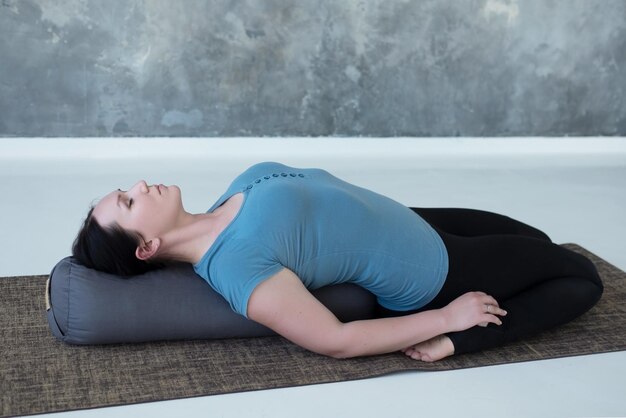 Cauacasian woman resting in reclining hero pose or Supta Virasana with bolster