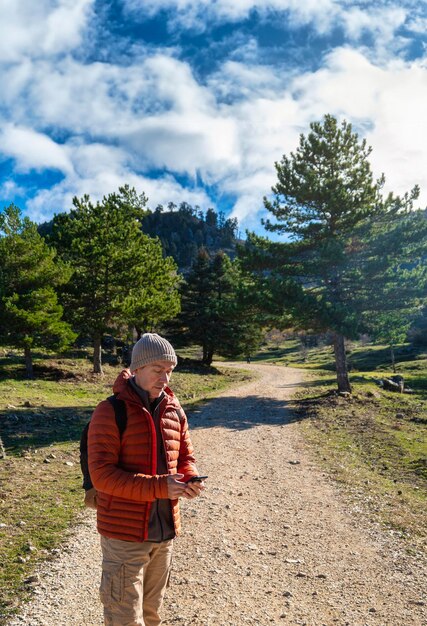 Caucasian adult hiker in orange jacket looking at his smartphone communication navigator gps