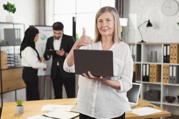 Caucasian aged woman with laptop posing at office