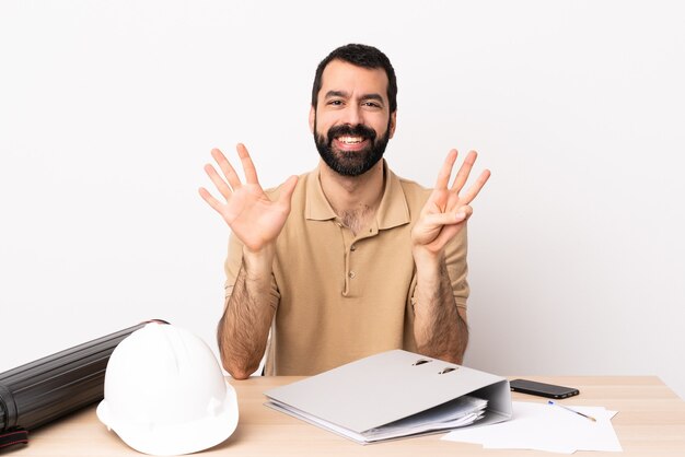 Uomo caucasico dell'architetto con la barba in una tabella che conta otto con le dita.