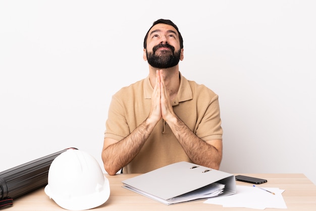 Caucasian architect man with beard in a table keeps palm together. Person asks for something