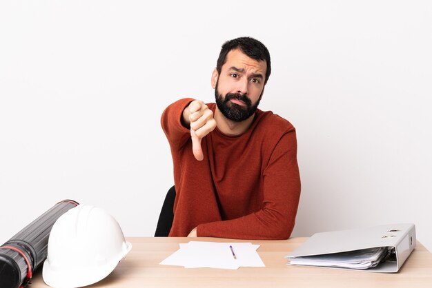 Caucasian architect man with beard in a table showing thumb down with negative expression.