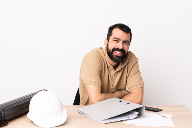 Caucasian architect man with beard in a table with arms crossed and looking forward.