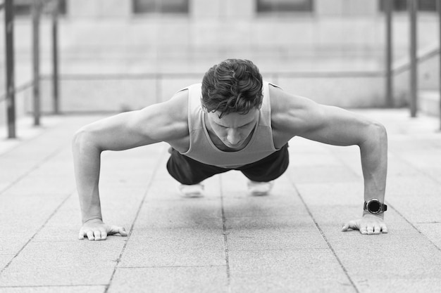 Atleta caucasico uomo che fa flessioni fitness uomo allenamento push up all'aperto giovane bell'uomo in abbigliamento sportivo facendo pushup facendo esercizi per polpacci e glutei bel ragazzo in forma che fa scricchiolii