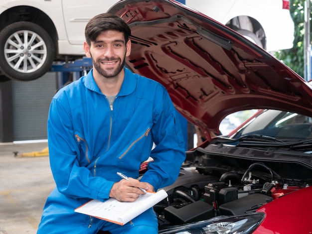 Caucasian auto mechanic in uniform holding clipboard of service order working in garage. technician checklist for repair machine a car in the garage.