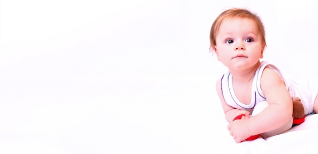 A caucasian baby boy lies in a white bodysuit with a toy on a white background