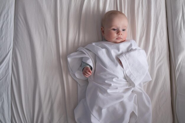ベッドに横たわっている父のTシャツに身を包んだ白人の赤ちゃん
