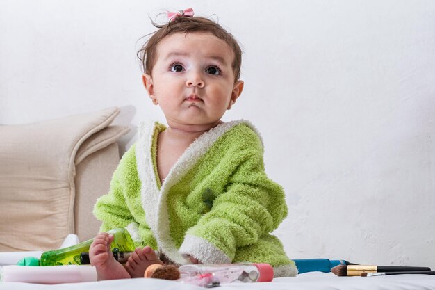 Caucasian baby sitting on the bed after having a bath girl with a green towel looking curiously