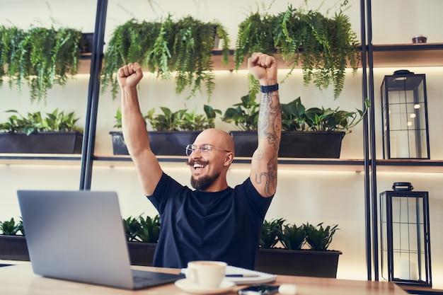 Photo caucasian bald man feels happy received good news by internet raised hands scream with joy