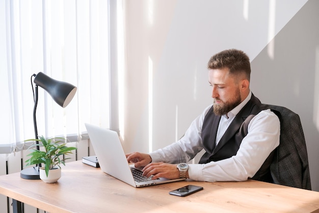 Caucasian bearded business man is sitting at window table using his laptop