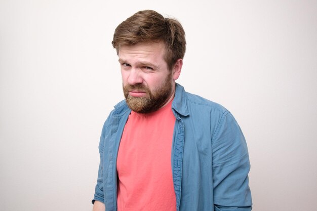 Photo caucasian bearded man distrustfully and contemptuously looks into the camera