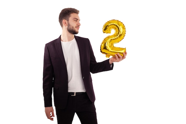 Caucasian bearded man holding a yellow balloon number two wearing a classic suit