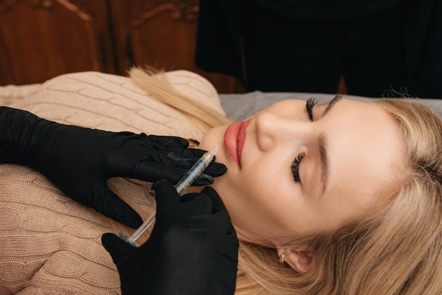 Caucasian beautiful blond hair woman receives procedure in spa salon for lip augmentation with geluronic acid. Beauty injections. close-up photo