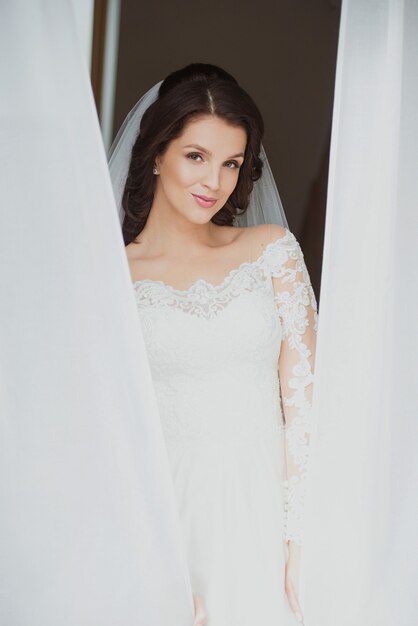 caucasian beautiful woman bride in traditional european white dress standing by the window