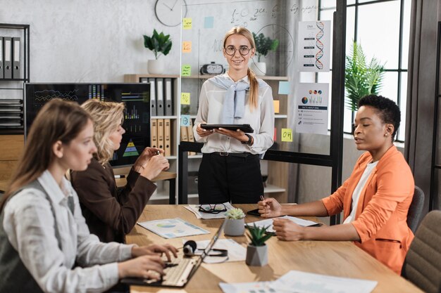 Caucasian blond woman with tablet in hands looking at camera while standing at office