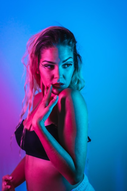 A caucasian blonde girl in a black t-shirt with eye drawing\
makeup, eyelashes arranged on a blue background with pink neon\
lights, having fun in a nightclub