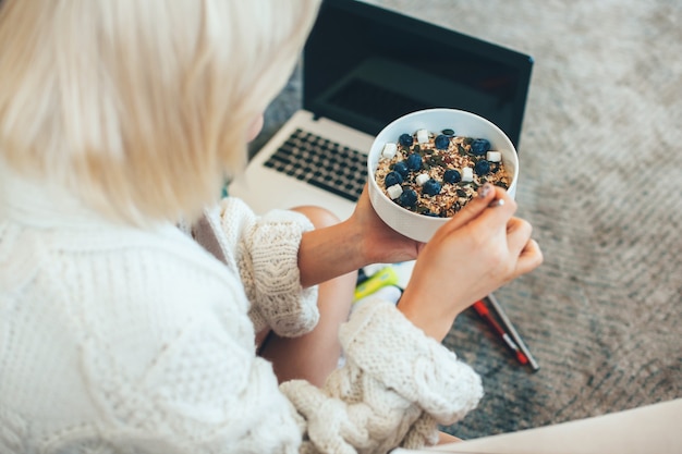 caucasian blonde lady eating cereals while working at the laptop on the floor