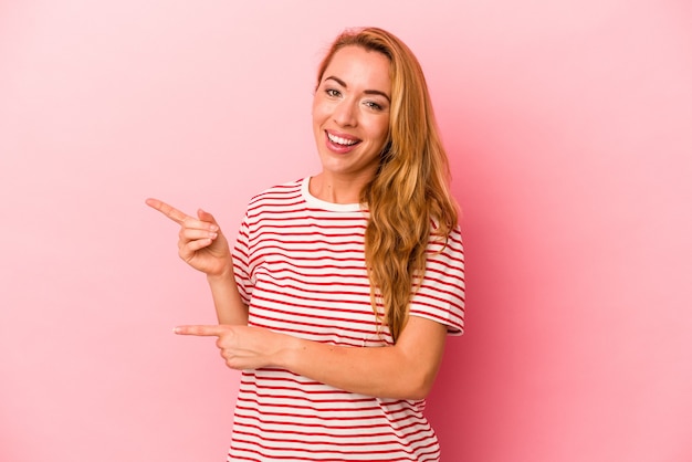 Caucasian blonde woman isolated on pink background excited pointing with forefingers away.