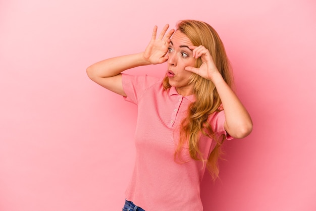 Caucasian blonde woman isolated on pink background keeping eyes opened to find a success opportunity.