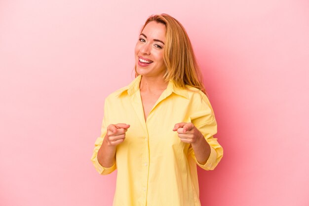 Caucasian blonde woman isolated on pink background pointing to front with fingers.