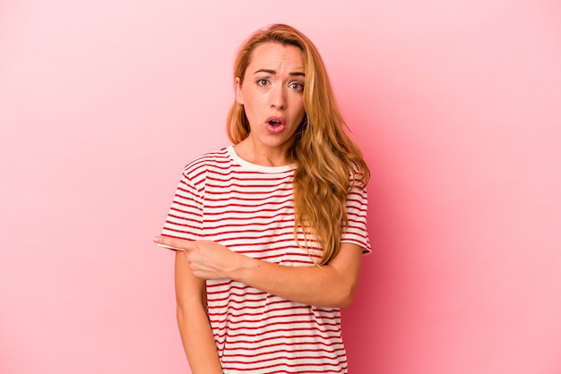 Caucasian blonde woman isolated on pink background pointing to the side